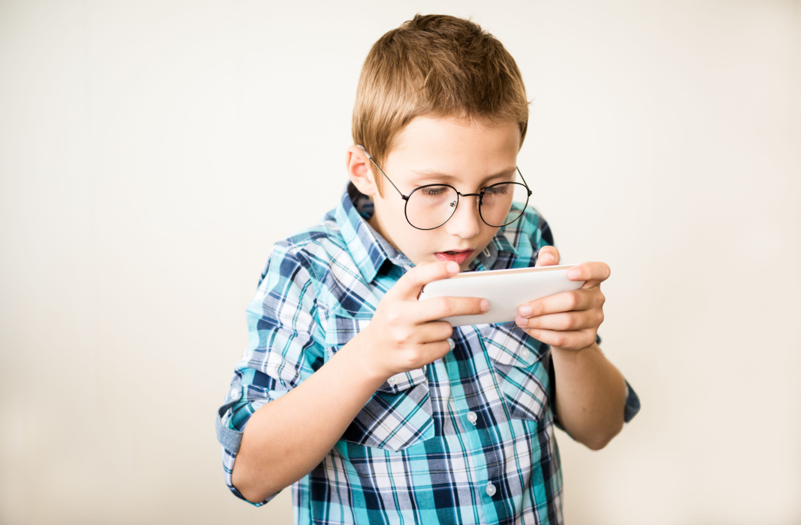 A child with large round glasses, standing and holding a smartphone very close to his face