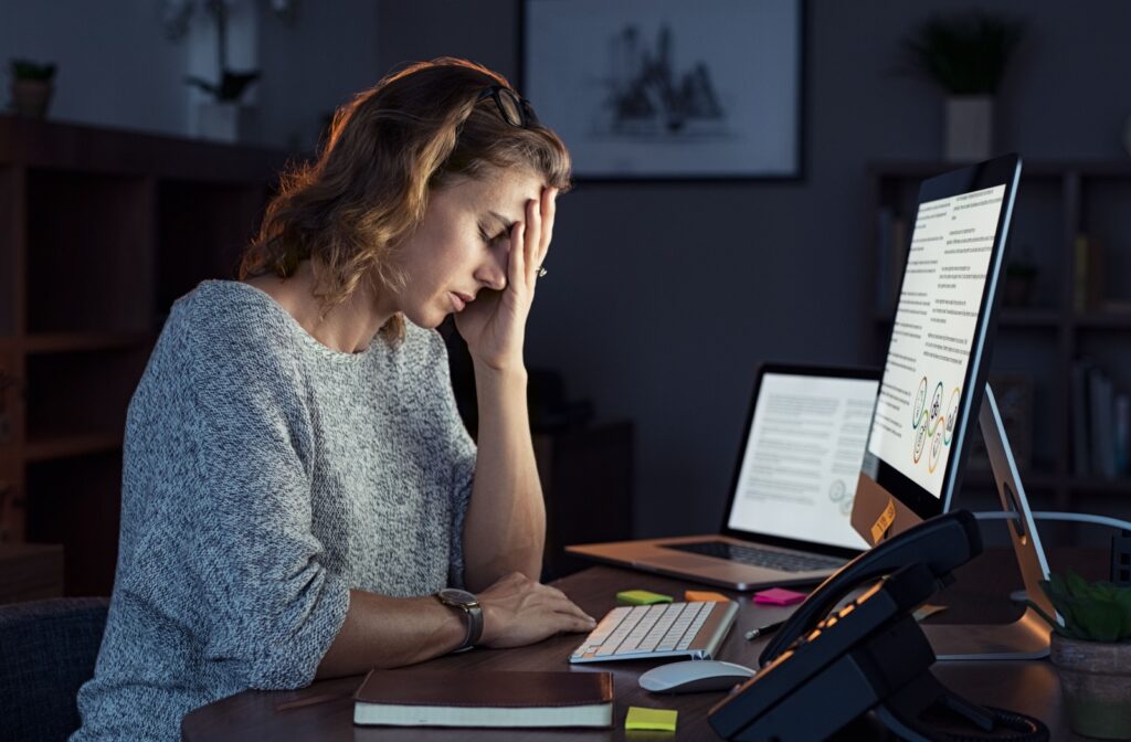 A young woman caressing her head as she experiences a headache while working on her computer.