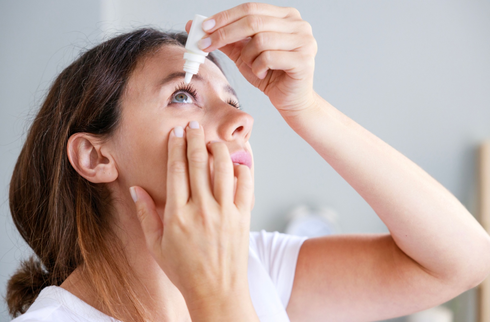 A young woman putting in artificial tears to find relief from dry eyes.