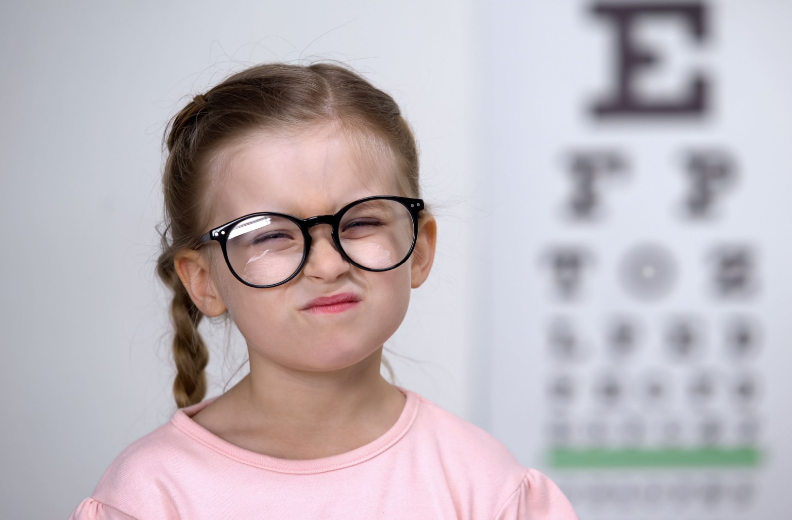 A little girl wearing glasses squinting during an eye exam due to her myopia.