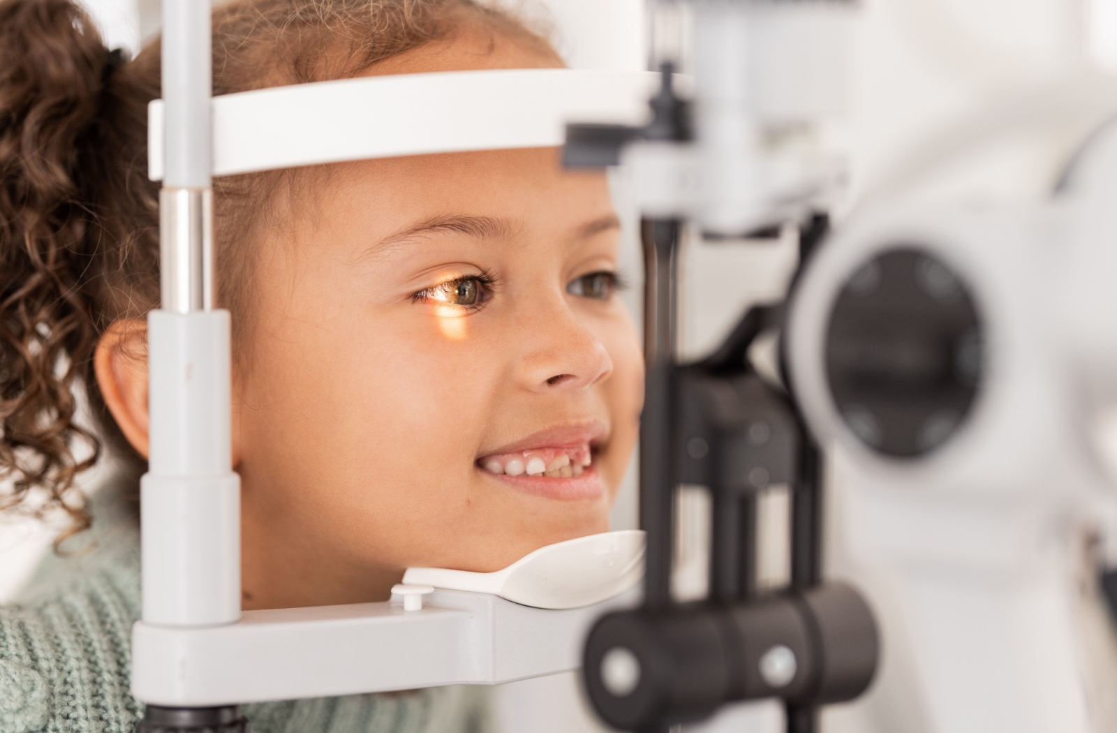 A child smiling during a slit-lamp eye exam to learn if myopia control can help her vision.