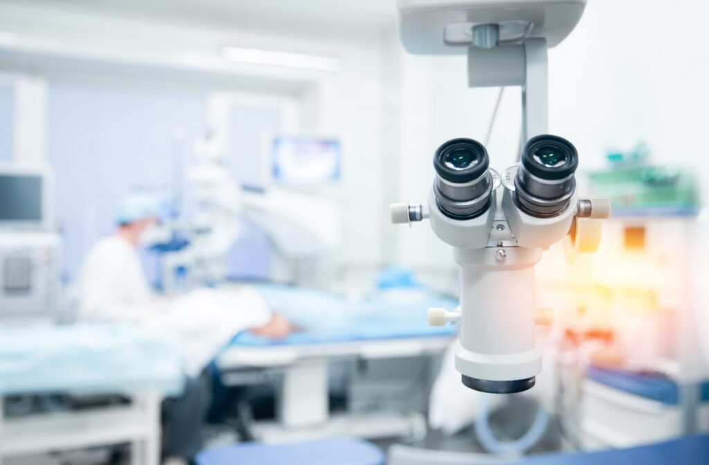 Close-up of a microscope, with a doctor performing eye surgery on patient in the partially blurred background.