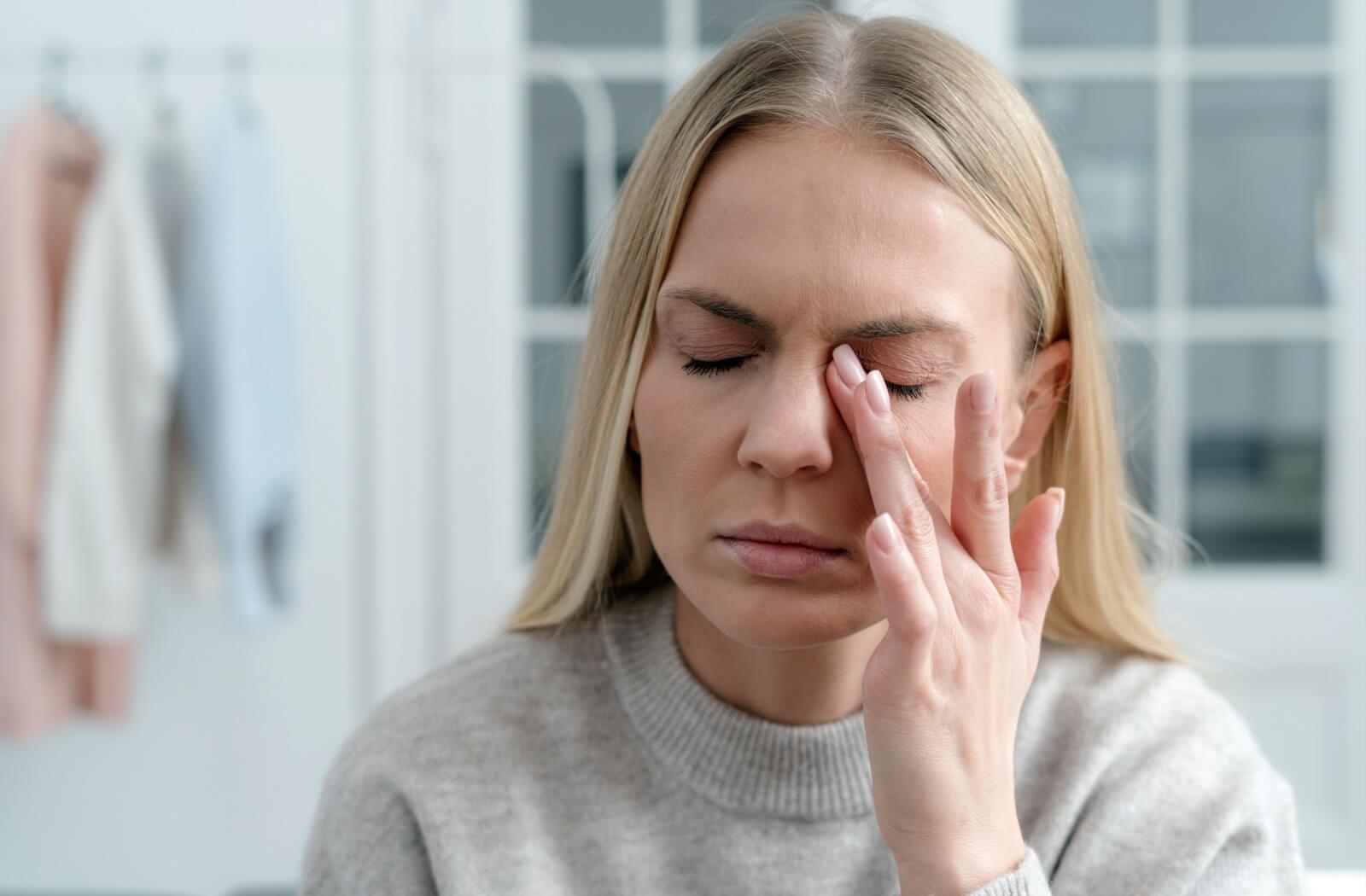 An adult rubs their eye, experiencing irritation from their contact lenses drying out.