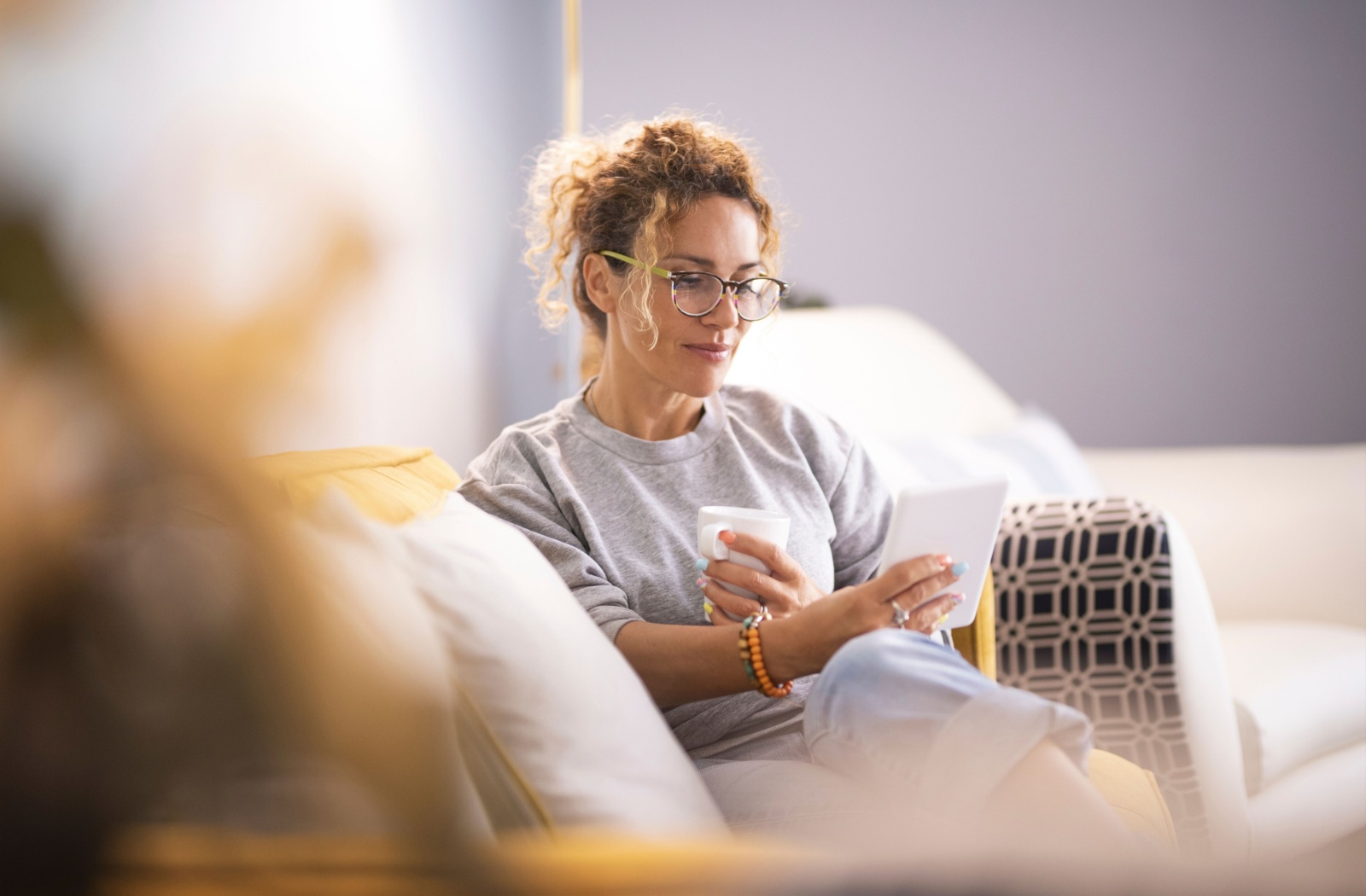 A person sitting on a couch during the day, enjoying a cup of coffee while reading an eBook.