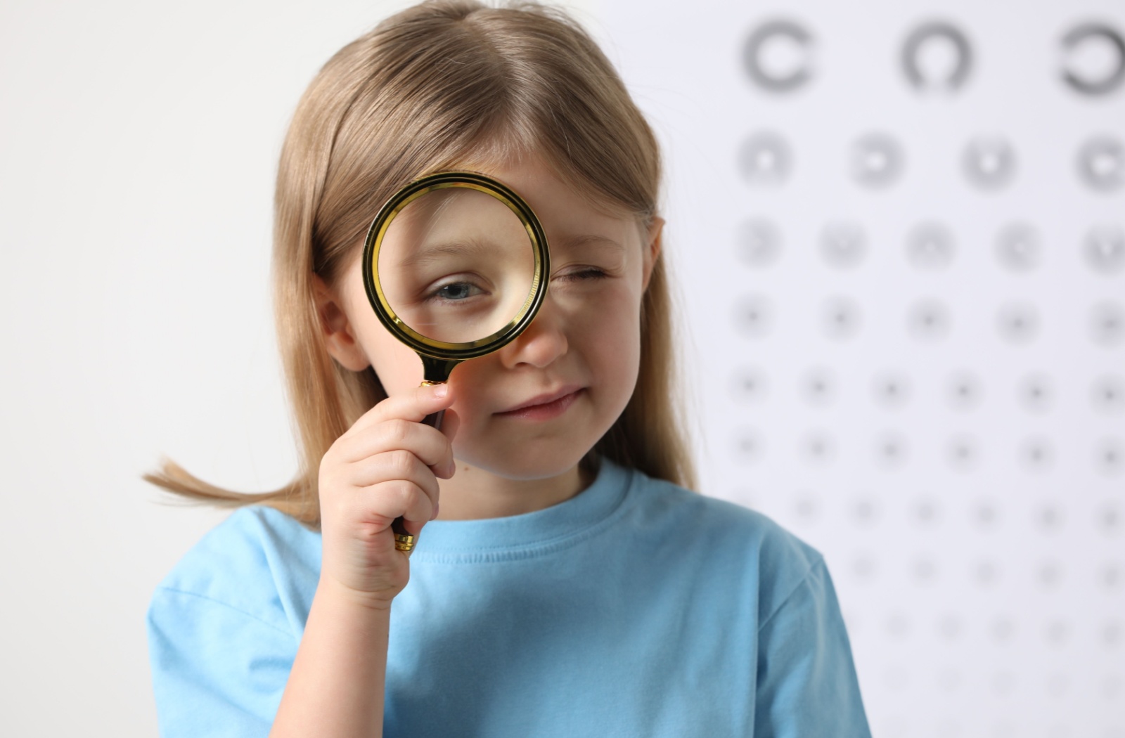 A child holding a magnifying glass in front of her eye, illustrating the concept of myopia.