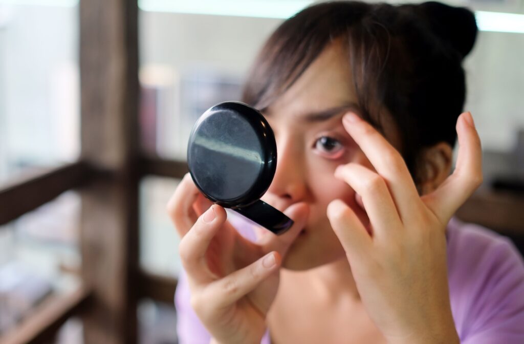 young adult gently pulling her eye wider to look at her eye using a compact mirror