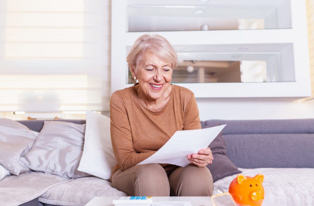 Smiling older adult sitting on a couch and reading a piece of paper without glasses.