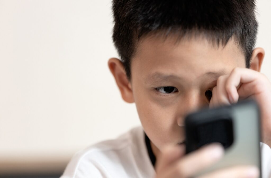 Child rubbing eye and while looking at smartphone.