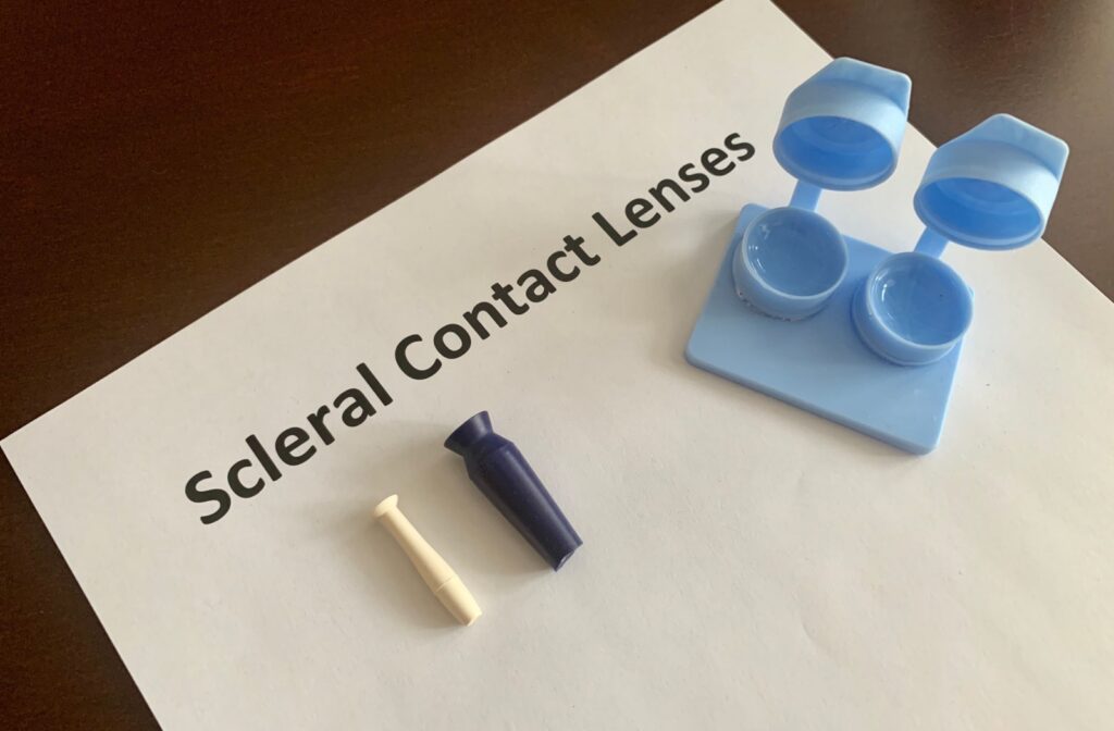 A blue contact lens case and 2 applicators on a sheet of paper that reads "Scleral Contact Lenses."