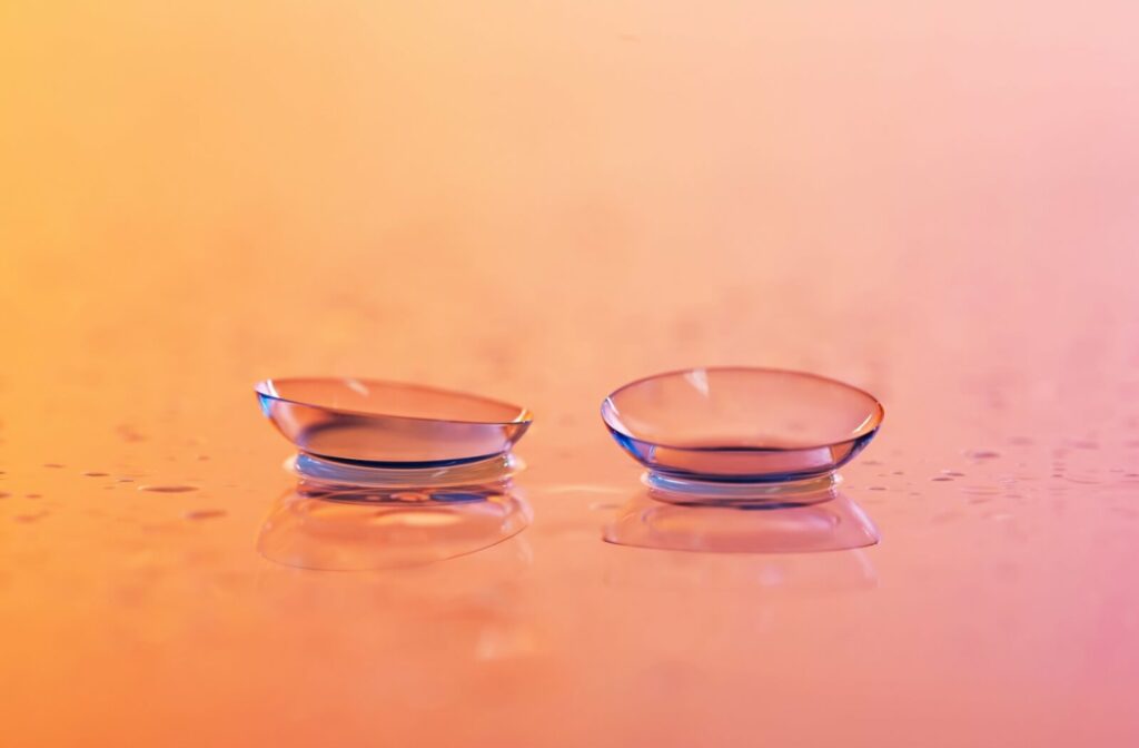 Two contact lenses resting on a reflective surface with an orange and pink gradient background, symbolizing vision correction and eye care for conditions like astigmatism.