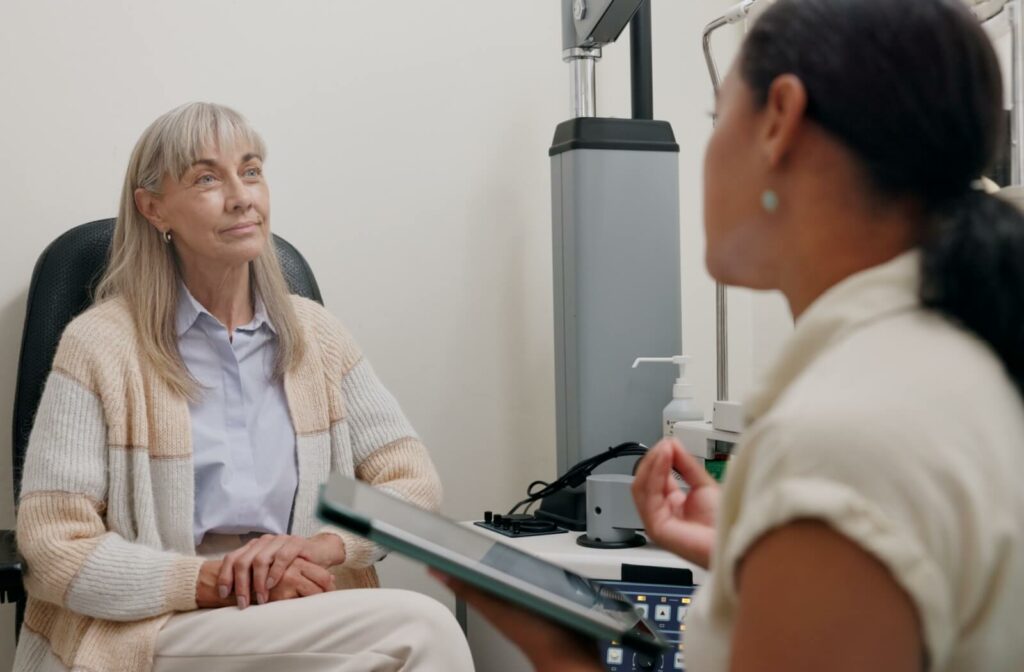 Optometrist discussing eye care options with an older woman during an eye exam, with diagnostic equipment visible in the background.