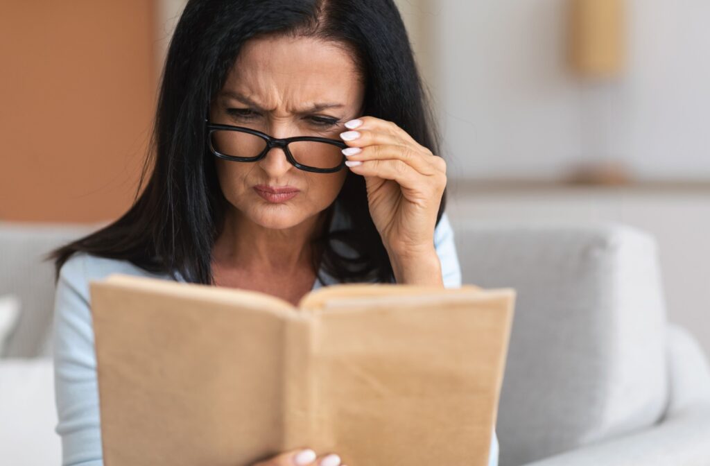 Close up a person reading a book and holding their glasses while squinting to see better