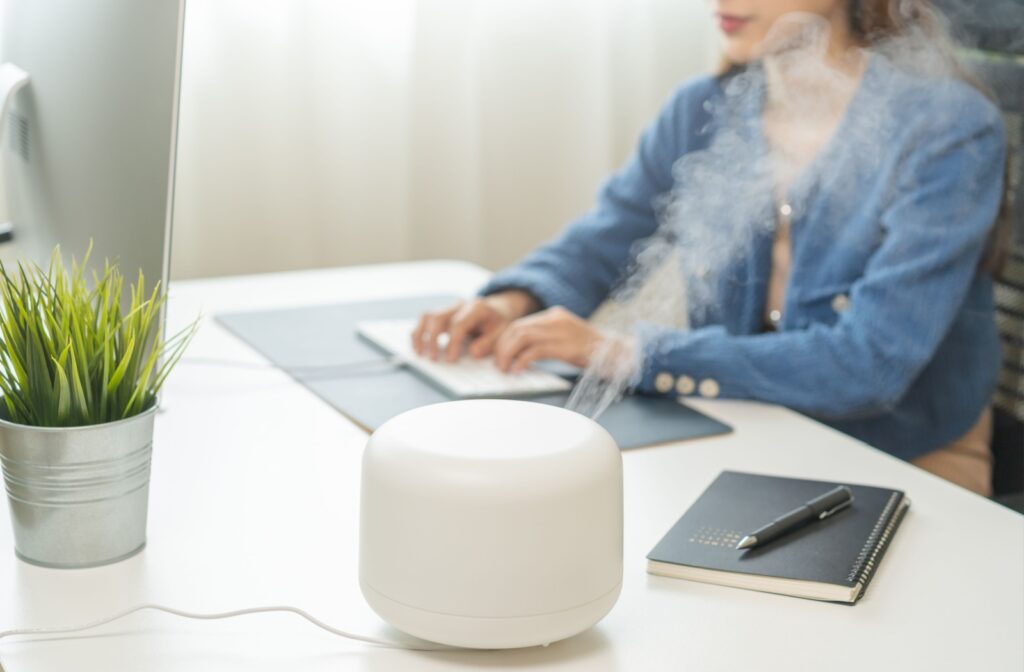 A white humidifier rests on a desk with a person in the background working on a computer