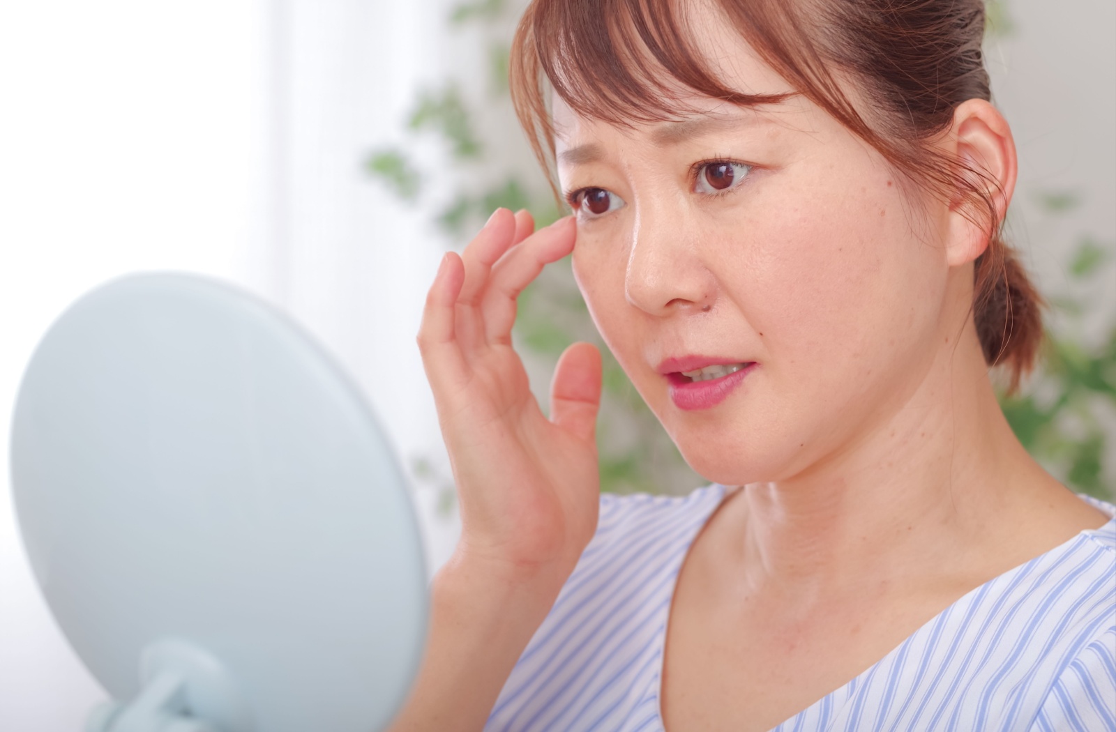A person looking at their eye using a hand held mirror