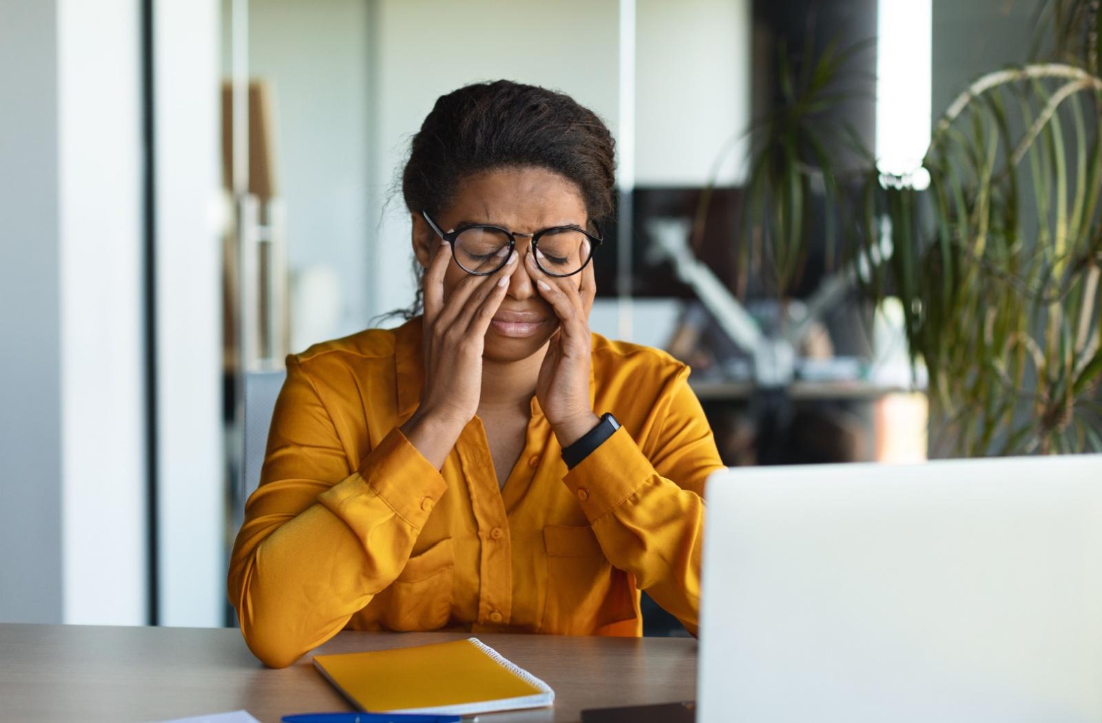 A person sitting in front of a computer and rubbing their dry eyes